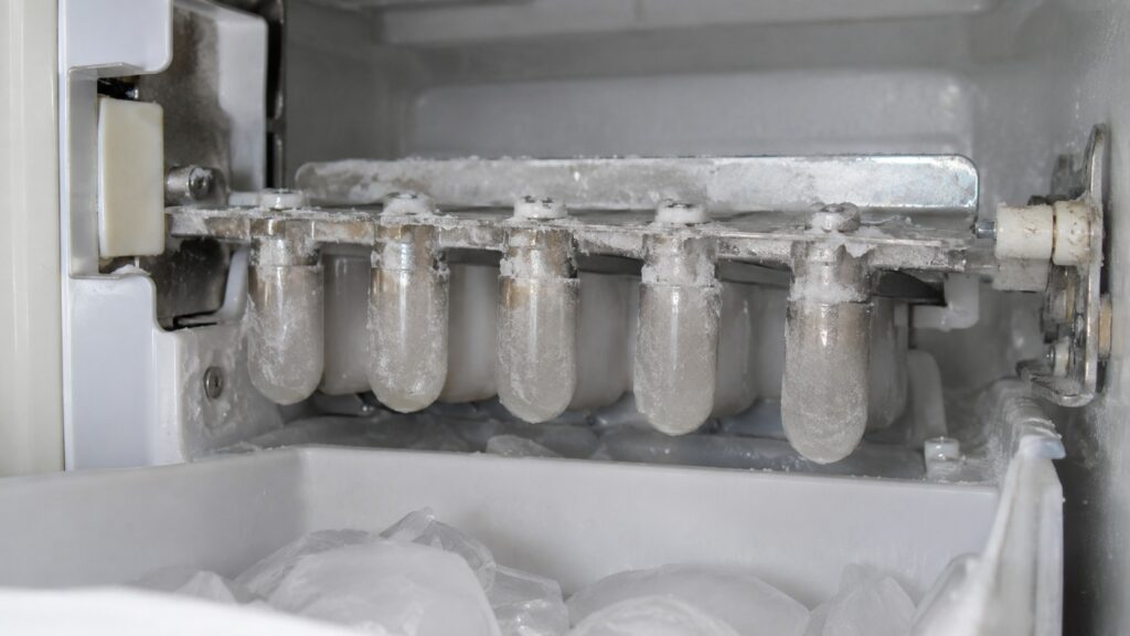 A close-up of an ice maker mold assembly inside a refrigerator with light white residue visible