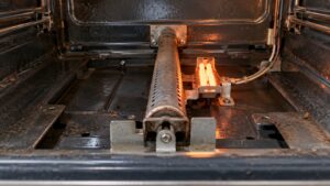 The bottom of a gas oven cavity with the bake burner tube and a glowing igniter beside it