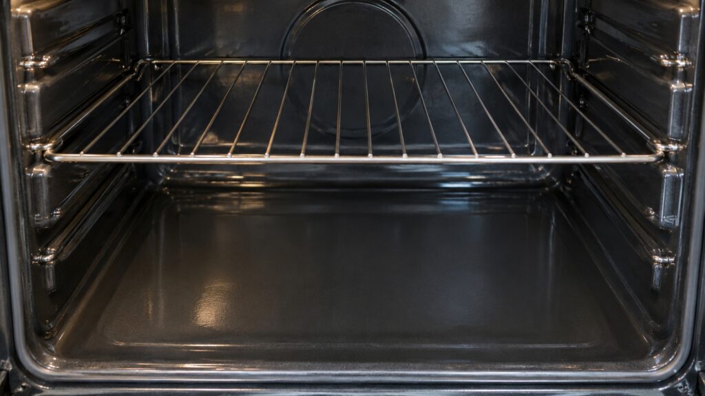 A close view of a smooth flat oven cavity floor with a single empty wire rack above it